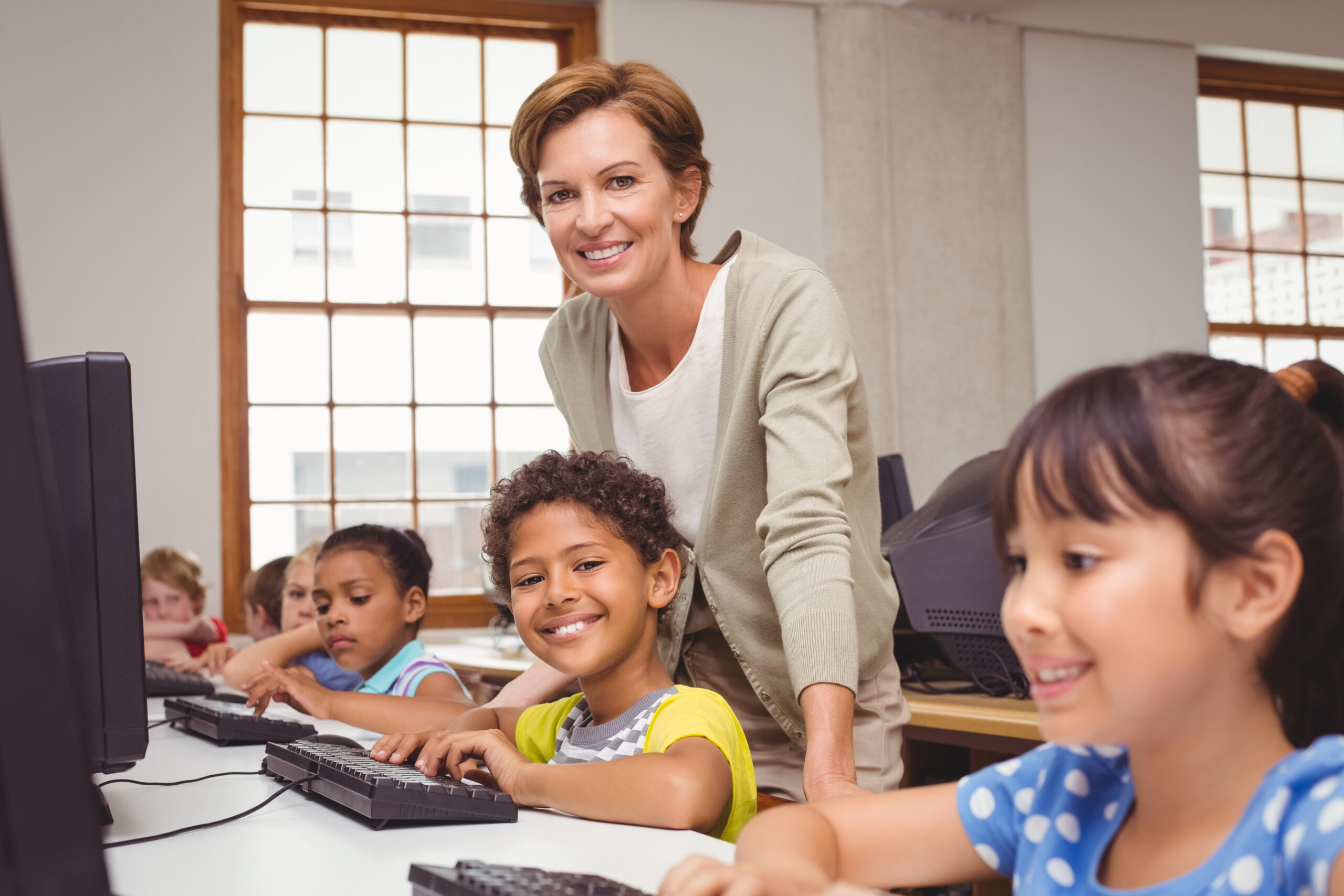 Cute,Pupil,In,Computer,Class,With,Teacher,Smiling,At,Camera